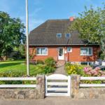 Rotes Haus mit Garten, Terrasse und Blumenbeeten. Weiße Zaun und Tor.