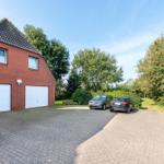 Rotes Backsteingebäude mit zwei Garagen und gepflastertem Vorplatz mit zwei Autos.