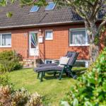 Rotes Backsteingebäude mit Garten und Liegestühlen unter Bäumen.