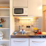 Küche mit Spüle, Herd und Mikrowelle. Regal mit Küchenutensilien und Kaffeefiltern.