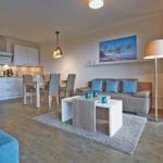 Wohn- und Essbereich mit Sofa, Tisch und Küchenzeile. Große Fenster und modern eingerichtet.