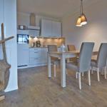 Essbereich mit Tisch und Stühlen, Küchenbereich im Hintergrund, Bodenbelag aus Holz, dekoratives Holzobjekt