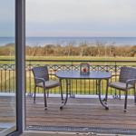 Terrasse mit Tisch und zwei Stühlen, Blick auf Meer und Grünfläche.