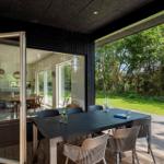 Terrasse mit Tisch und Stühlen, Blick auf grünen Garten und Wald. Tür führt ins Haus.