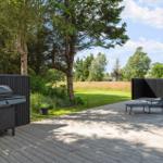 Terrasse mit Grill und Liegestühlen, umgeben von Grün und Bäumen.