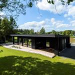 Moderne schwarze Hütte mit großem Glasbereich und Terrasse im Grünen.