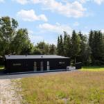 Moderne schwarze Hütte mit Glasfenstern in grüner Umgebung.