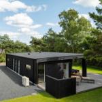 Moderne schwarze Villa mit Terrasse und Garten. Holzterrasse mit Liege und Tisch.