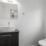 Badezimmer mit Waschbecken, Spiegel und Toilette. Fenster mit Pflanze.