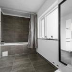 Badezimmer mit Badewanne, Fenster und Spiegel.
