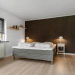 Schlafzimmer mit Bett, Nachttisch und Fenster. Wand mit strukturiertem Tapetenmuster.