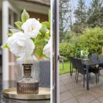 Terrasse mit Tisch und Stühlen, Blumenarrangement und Blick auf grüne Hecke.