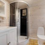 Bathroom with shower, sink and toilet against wooden wall