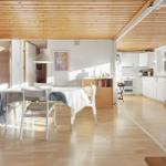 Living kitchen with dining table, white chairs, and wooden ceiling.