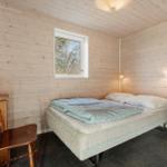 Bedroom with bed, chair, and window. Wooden walls and white furniture.