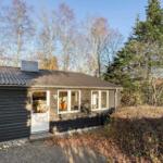 A house with dark siding and solar panel on roof. Surrounded by trees and shrubs.