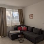 Wohnzimmer mit Ecksofa, Fenster und Blick in Schlafzimmer.