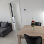 Essbereich mit Tisch und Stühlen, daneben Wohnbereich mit Sofa und Tür zum Schlafzimmer.