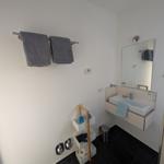 Badezimmer mit Waschbecken, Spiegel, Handtuchhalter und Aufbewahrungsregal.