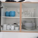 Küchenschrank mit Tassen, Tellern, Gläsern und blauen Schüsseln.