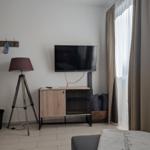 Wohnzimmer mit Fernseher, Stehlampe und Fenster mit Vorhängen.