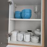 Schrank mit blauen Schüsseln, Weingläsern und weißer Tasse, Teller und Teekanne.