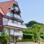 Zweistöckiges Haus mit Balkonen und rotem Dach, umgeben von Grünflächen.