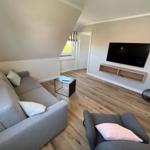 Wohnzimmer mit Sofa, Sessel, Fernseher und Holzboden.