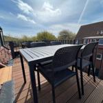 Terrasse mit Tisch und Stühlen, Blick auf Wohnhäuser und Bäume.