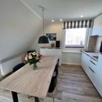 Essbereich mit Tisch, Stühlen und Blumen. Küche mit Arbeitsplatte und Fenster.