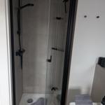 Duschkabine mit Glaswand und schwarzen Armaturen. Handtuch und Pflegeprodukte sind vorhanden.