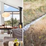 Modern dining room with large windows and fireplace. Outside view shows a small stream.