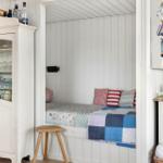 Bedroom with bed, pillows, and wooden stool. Beside it stands a white cabinet with glass.