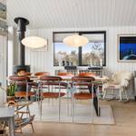 Dining room with wooden table, chairs, and fireplace. Windows overlook green areas.