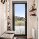 Entrance with door to wooden terrace and green area. Wall shelves and bench.