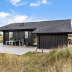 Black house with terrace and garden. Table, chairs, and grill are present.