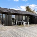 Modern wooden cabin with terrace, table, and chairs. Background: sky and trees.