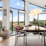 Dining room with wooden table, leather chairs, and fireplace. Large windows overlook grassland.