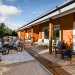 Terrace with lounge area, seating group, and sun loungers beside wooden house with glass front.