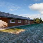 Modern wooden house with frost-covered lawn and view of forest.