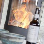 A fireplace with burning logs, a bottle and glasses on a table.