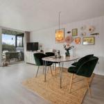 Dining area with green chairs and table on rug. Glass doors lead to terrace with garden.