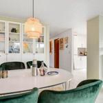 Dining area with round table, green chairs, and wood stove against wall.