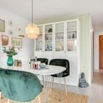 Dining area with round table, green chairs, and glass cabinet.