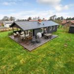 A house with terrace, garden, and garden furniture under blue sky.
