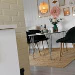 Dining table with four green chairs on rug against white wall.