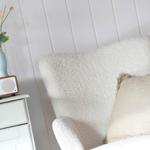 White armchair with cushion, beside nightstand with radio and vase flowers.
