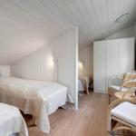 Room with two beds, wardrobe, and seating. Wooden floor and white paneled walls.
