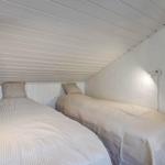 Two single beds under a sloped ceiling with wall lamps and plants.