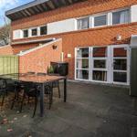 Backyard with table, chairs, and patio area. House with red brick and white windows.